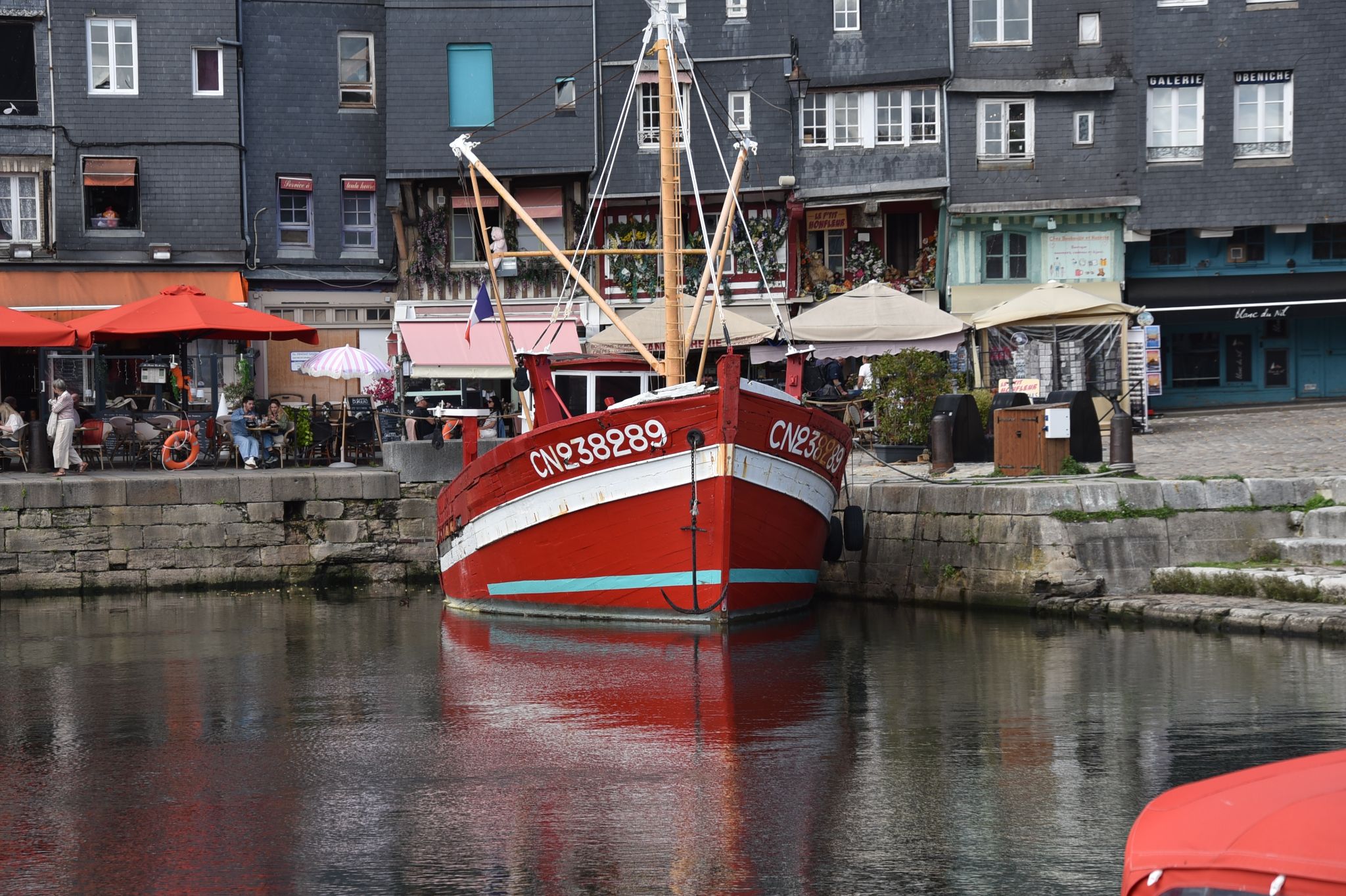 A bright red and white wooden fishing boat moored in the historic Vieux Bassin (Old Harbor) of Honfleur, Normandy, France